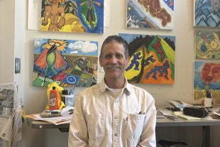 Physics Professor Tony Garcia, who specializes in geology, poses in his office with his art work in the background.