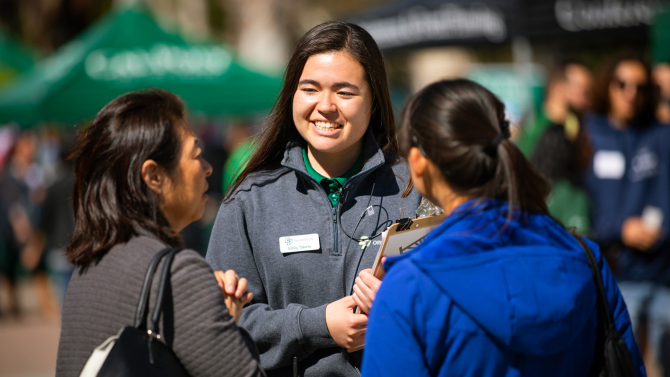 Student guide talks to a parent and prospective student at an event