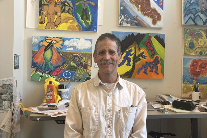 Physics Professor Tony Garcia, who specializes in geology, poses in his office with his art work in the background.