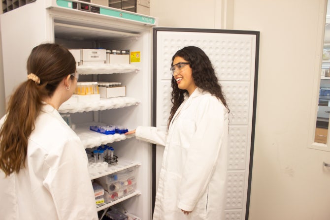 Two students wearing lab coats and safety goggles stand near frozen samples in a Frost Center lab.