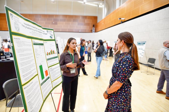 A student presents their poster to a professor at a research poster session.
